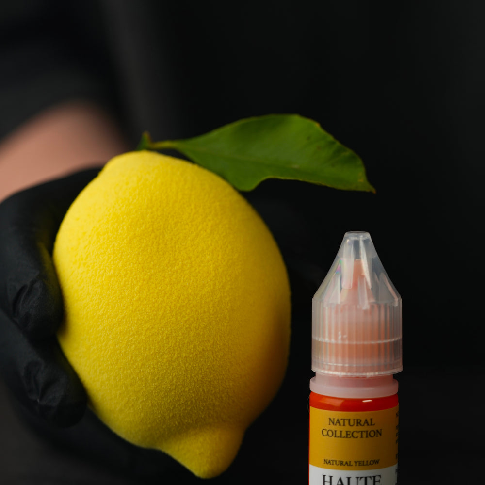 Yellow lemon held by a gloved hand next to a bottle labeled 'HAUTE'. Best Natural Haute Food Colors by Ksenia Penkina, Vegetable Colours, Liquid Gel, Water Soluble, Oil Soluble, Fat Soluble Gel, Food Colouring, Chefrubber, Colourmill, Chefmaster, Silikomart, Pavoni, Decorelief, Matfer, PastryClass, Valrhona, Cacao Barry, For Macarons, For Glazing